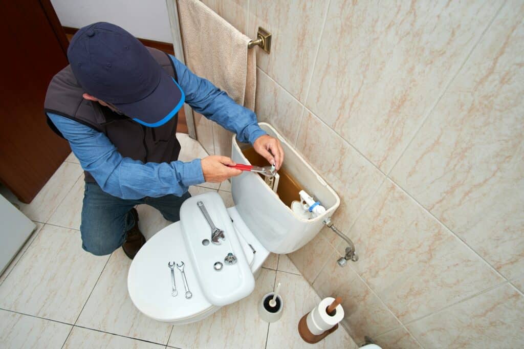Plombier en intervention sur le réservoir d'une chasse d'eau dans une salle de bain